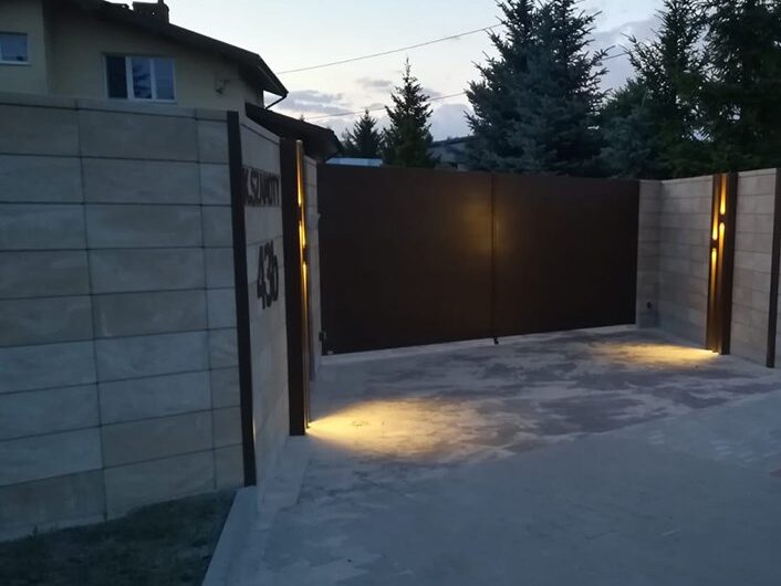 Aluminiowa brama oświetlona wieczorem.