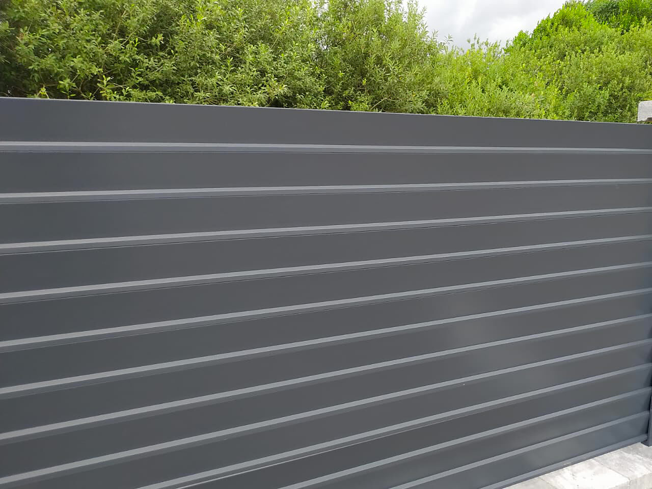 Przykład nowoczesnego ogrodzenia aluminiowego panelowego, zapewniającego pełną prywatność i przepływ powietrza dzięki skośnie zainstalowanym panelom.