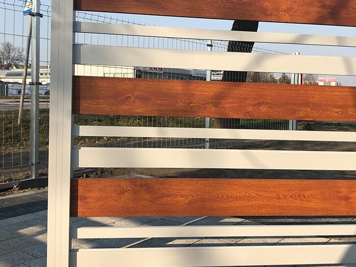 Na zdjęciu ogrodzenie aluminiowe z elementami imitacji drewna, kolory biały i czerwony.