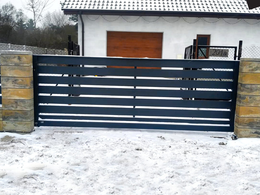 Ogrodzenia aluminiowe sprawdzają się świetnie w różnych warunkach pogodowych. Na zdjęciu przykład ogrodzenia aluminiowego kolor antracyt, które prezentuje się wspaniale - i czysto - na tle śniegu.